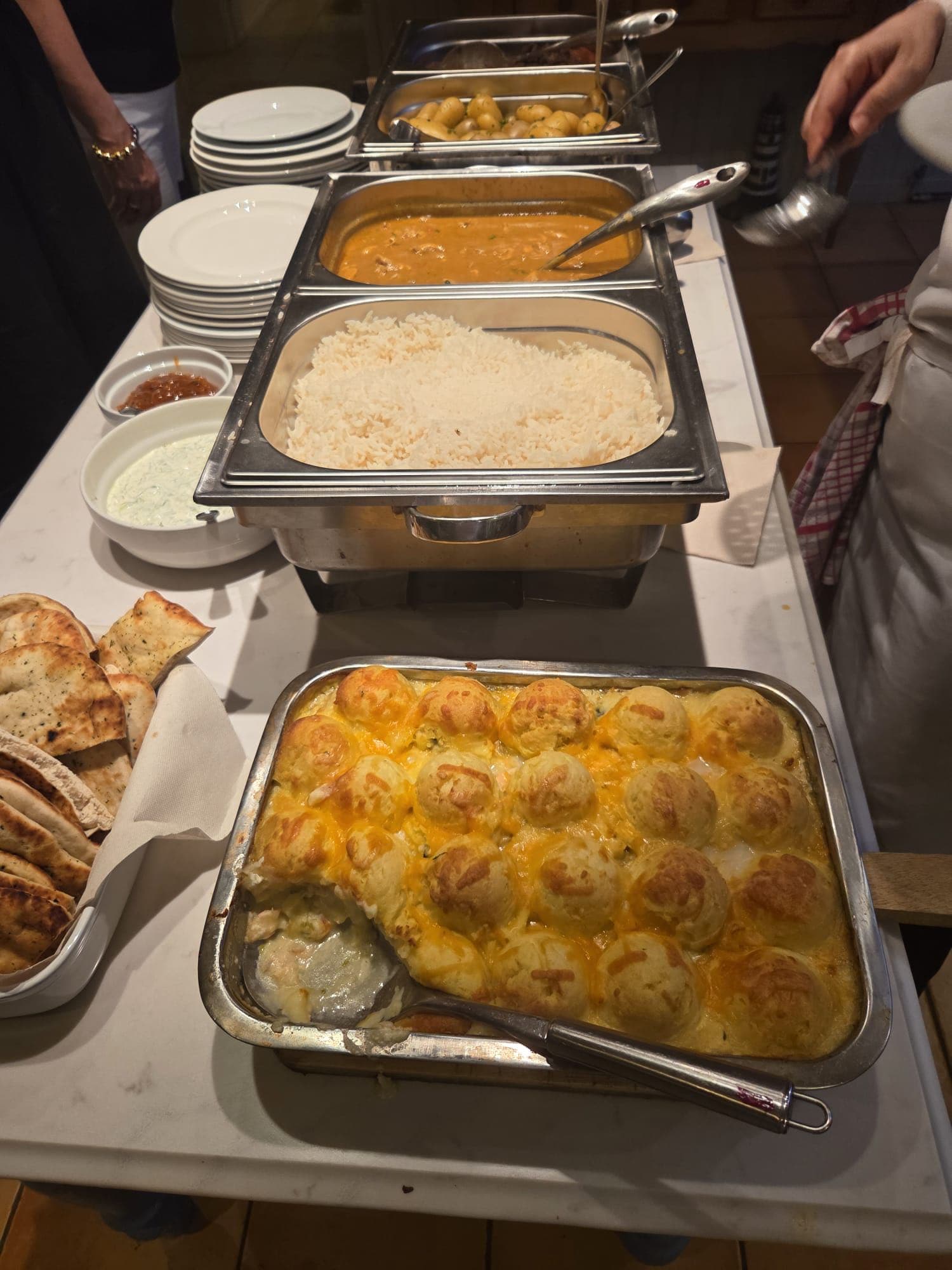 A three-dish buffet station mid-event — curry and rice, a fish bake, and pita bread arranged in chafing dishes.